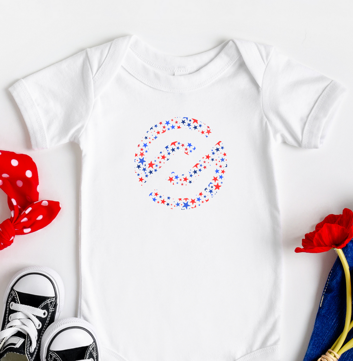Baby onesie with colorful design, black sneakers, red polka dot headband, blue pants, and red flowers on a white background