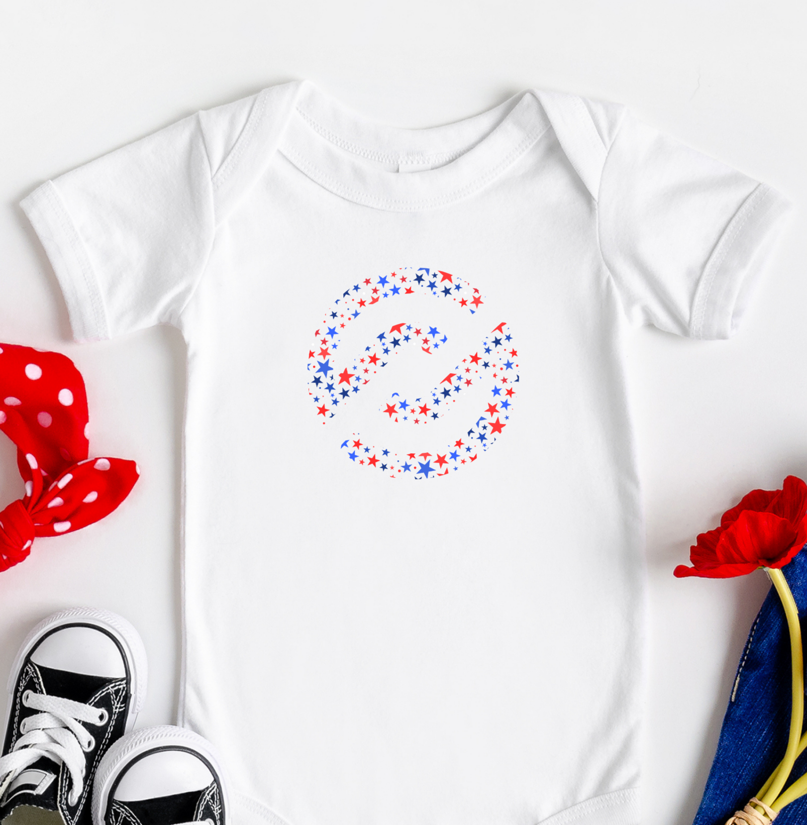 Baby onesie with colorful design, black sneakers, red polka dot headband, blue pants, and red flowers on a white background