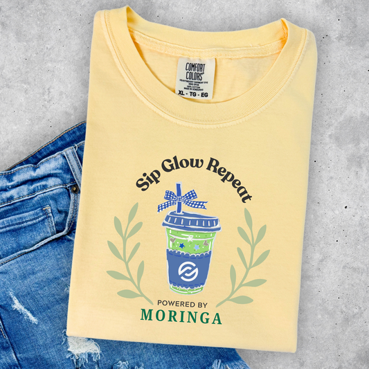 Preppy Sip Glow Repeat graphic featuring an iced Moringa tea cup with blue bow accent printed on a Comfort Colors Butter yellow t-shirt for the PartnerCo Moringa launch.